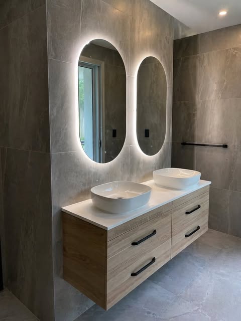 Two illuminated oval mirrors above a timber bathroom vanity